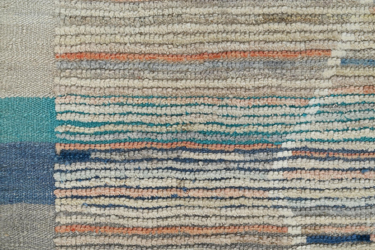 Close-up of a woven rug or textile with horizontal striped patterns in beige, cream, gray, teal, blue, and muted coral. Atlantica Organics curates antique and handmade rugs, Persian, Afghan, Tibetan, Pakistani, Turkish Oushak, Kilim, Khotan, tribal and contemporary textiles for luxury interiors, homes and real estate. Our collections connect timeless craftsmanship with interior design, furniture, fine art, architecture and modern living. Explore curated rugs, collectible textiles, natural materials, cultura
