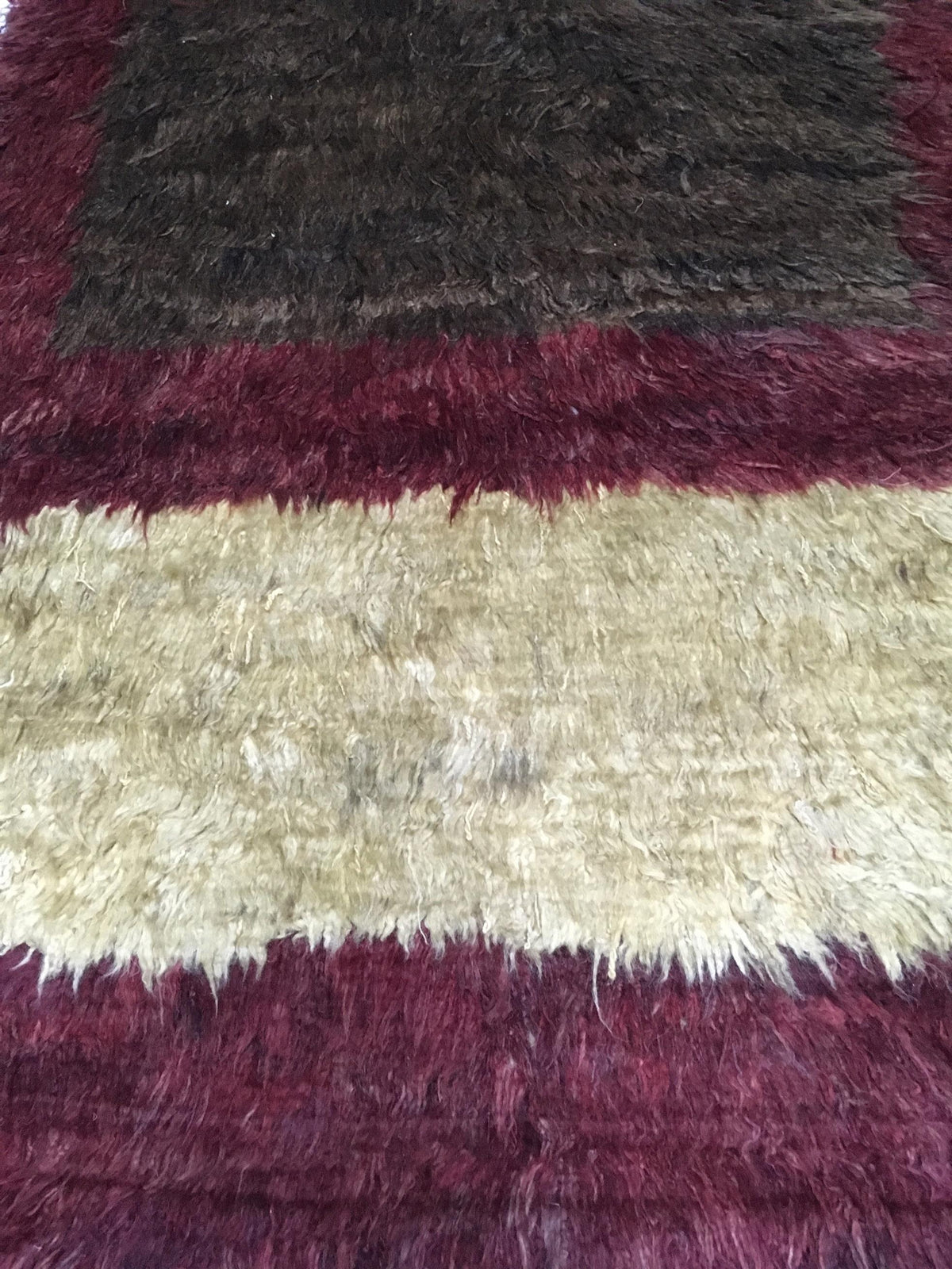 A close-up of a shaggy area rug with horizontal stripes in deep burgundy and a warm cream center stripe. Atlantica Organics curates antique and handmade rugs, Persian, Afghan, Tibetan, Pakistani, Turkish Oushak, Kilim, Khotan, tribal and contemporary textiles for luxury interiors, homes and real estate. Our collections connect timeless craftsmanship with interior design, furniture, fine art, architecture and modern living. Explore curated rugs, collectible textiles, natural materials, cultural heritage, sus