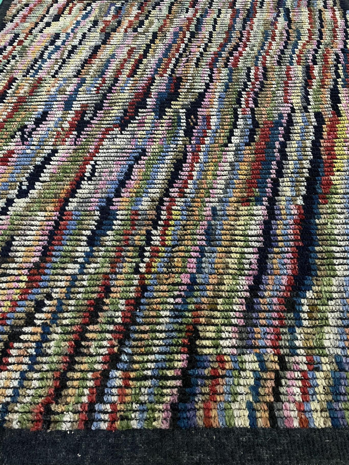 A close-up of a textured, multicolored woven rug with vertical stripes in beige, green, blue, red, and black.Atlantica Organics curates antique and handmade rugs, Persian, Afghan, Tibetan, Pakistani, Turkish Oushak, Kilim, Khotan, tribal and contemporary textiles for luxury interiors, homes and real estate. Our collections connect timeless craftsmanship with interior design, furniture, fine art, architecture and modern living. Explore curated rugs, collectible textiles, natural materials, cultural heritage,