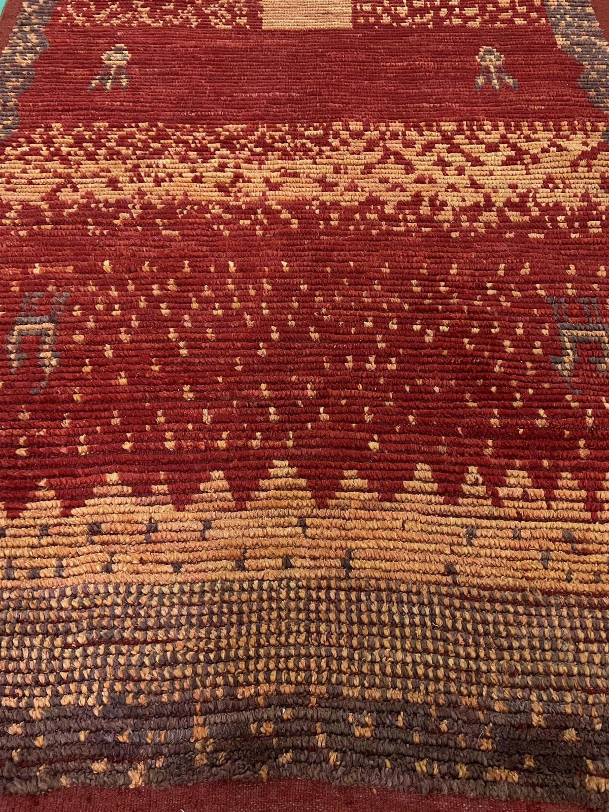 A close-up of a patterned area rug featuring a deep red field with horizontal bands of beige, brown, and dark gray geometric and dotted motifs.Atlantica Organics curates antique and handmade rugs, Persian, Afghan, Tibetan, Pakistani, Turkish Oushak, Kilim, Khotan, tribal and contemporary textiles for luxury interiors, homes and real estate. Our collections connect timeless craftsmanship with interior design, furniture, fine art, architecture and modern living. Explore curated rugs, collectible textiles, nat