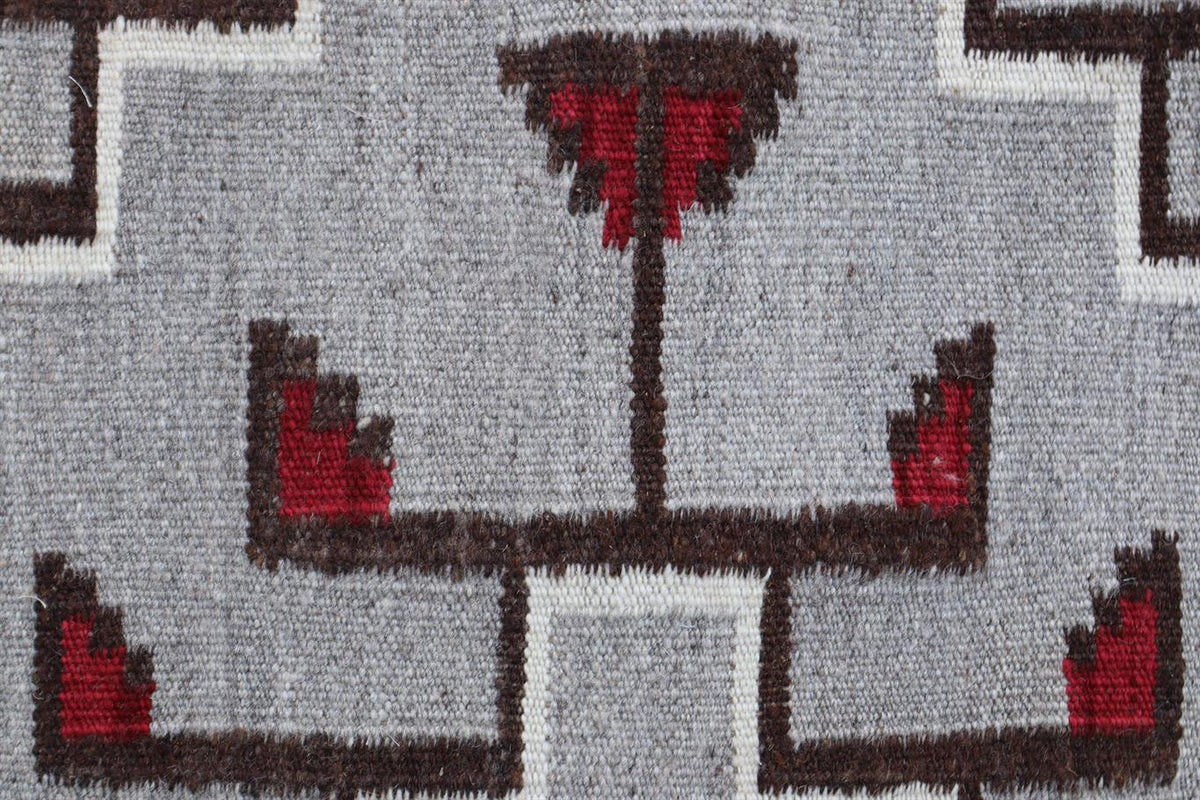 A close-up of a woven textile pattern featuring a gray background with dark brown geometric lines and red accents. Atlantica Organics curates antique and handmade rugs, Persian, Afghan, Tibetan, Pakistani, Turkish Oushak, Kilim, Khotan, tribal and contemporary textiles for luxury interiors, homes and real estate. Our collections connect timeless craftsmanship with interior design, furniture, fine art, architecture and modern living. Explore curated rugs, collectible textiles, natural materials, cultural her