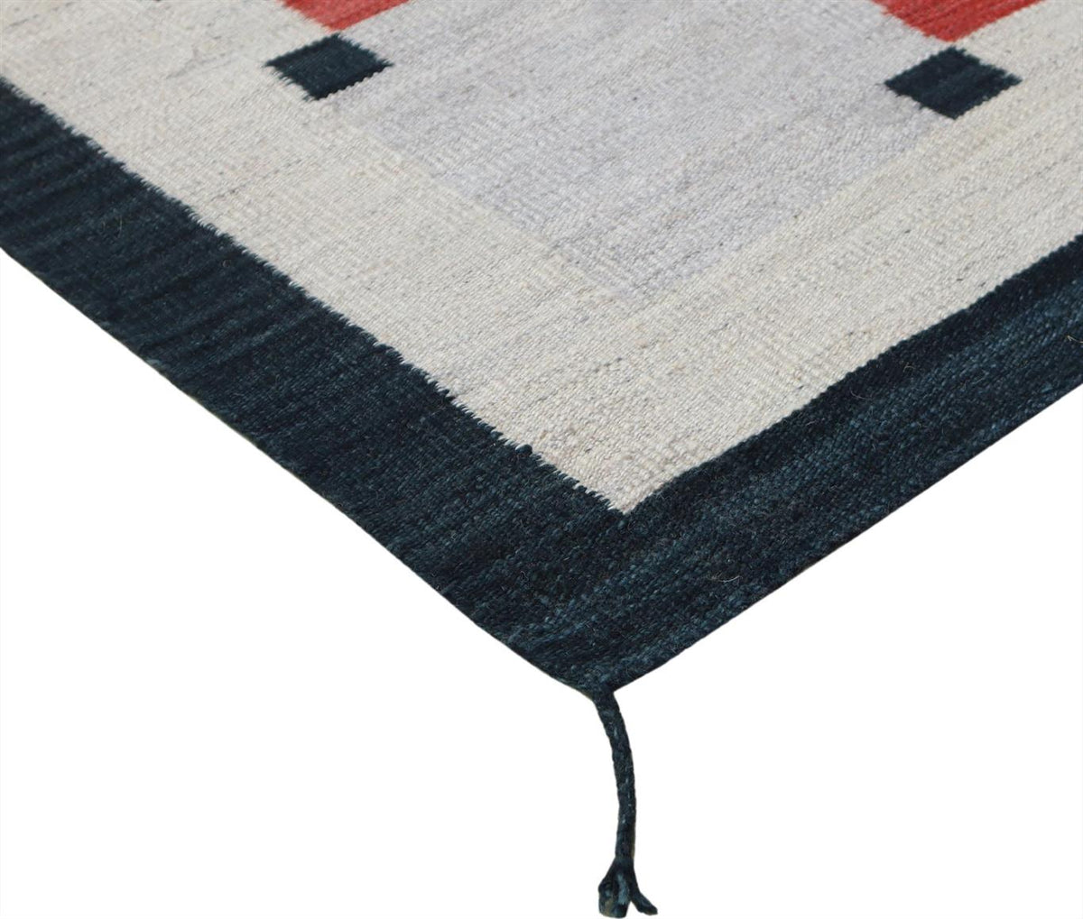 A close-up of a woven rug corner showing a dark navy border, a light gray field, and small red and navy geometric accents. Atlantica Organics curates antique and handmade rugs, Persian, Afghan, Tibetan, Pakistani, Turkish Oushak, Kilim, Khotan, tribal and contemporary textiles for luxury interiors, homes and real estate. Our collections connect timeless craftsmanship with interior design, furniture, fine art, architecture and modern living. Explore curated rugs, collectible textiles, natural materials, cult