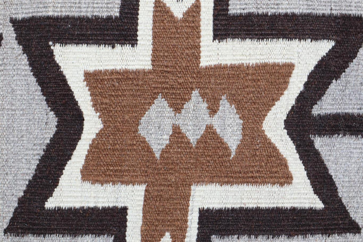 Close-up of a woven textile pattern with a geometric star-like design in brown, white, and dark charcoal gray. Atlantica Organics curates antique and handmade rugs, Persian, Afghan, Tibetan, Pakistani, Turkish Oushak, Kilim, Khotan, tribal and contemporary textiles for luxury interiors, homes and real estate. Our collections connect timeless craftsmanship with interior design, furniture, fine art, architecture and modern living. Explore curated rugs, collectible textiles, natural materials, cultural heritag