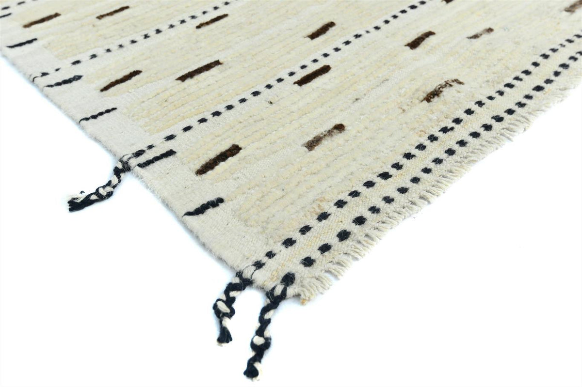 A close-up of a woven rug corner showing an off-white base with black dotted lines, small dark rectangular accents, and fringed tassels on a white background. Atlantica Organics curates antique and handmade rugs, Persian, Afghan, Tibetan, Pakistani, Turkish Oushak, Kilim, Khotan, tribal and contemporary textiles for luxury interiors, homes and real estate. Our collections connect timeless craftsmanship with interior design, furniture, fine art, architecture and modern living. Explore curated rugs, collectib