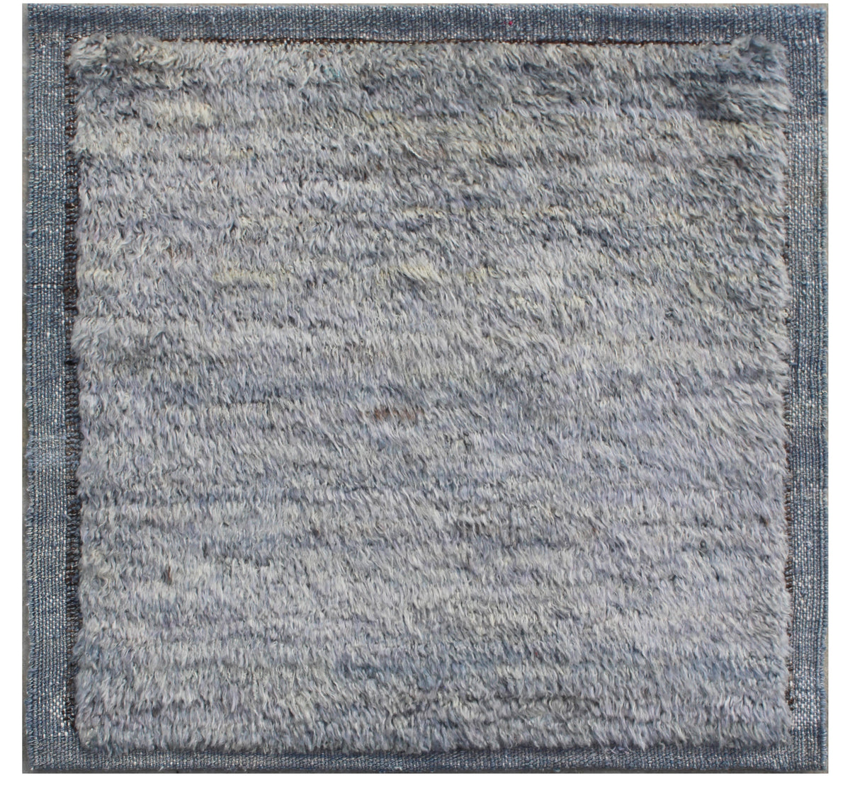 A square area rug with a thick, shaggy, textured pile in a light blue-gray color, finished with a contrasting medium-gray woven border. Atlantica Organics curates antique and handmade rugs, Persian, Afghan, Tibetan, Pakistani, Turkish Oushak, Kilim, Khotan, tribal and contemporary textiles for luxury interiors, homes and real estate. Our collections connect timeless craftsmanship with interior design, furniture, fine art, architecture and modern living. Explore curated rugs, collectible textiles, natural ma