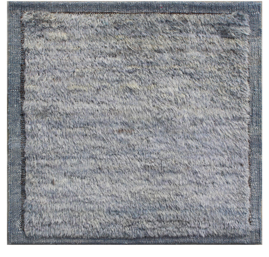 A square area rug with a thick, shaggy, textured pile in a light blue-gray color, finished with a contrasting medium-gray woven border. Atlantica Organics curates antique and handmade rugs, Persian, Afghan, Tibetan, Pakistani, Turkish Oushak, Kilim, Khotan, tribal and contemporary textiles for luxury interiors, homes and real estate. Our collections connect timeless craftsmanship with interior design, furniture, fine art, architecture and modern living. Explore curated rugs, collectible textiles, natural ma
