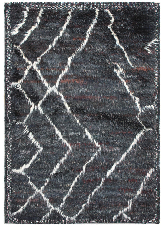 A rectangular shag area rug with a dark charcoal gray base, featuring a bold white zigzag diamond pattern and subtle rust-brown accents. Atlantica Organics curates antique and handmade rugs, Persian, Afghan, Tibetan, Pakistani, Turkish Oushak, Kilim, Khotan, tribal and contemporary textiles for luxury interiors, homes and real estate. Our collections connect timeless craftsmanship with interior design, furniture, fine art, architecture and modern living. Explore curated rugs, collectible textiles, natural m