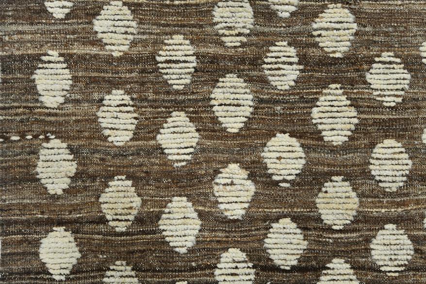 A close-up of a woven rug or textile with a brown base and repeating cream oval motifs in a textured, hand-knotted pattern. Atlantica Organics curates antique and handmade rugs, Persian, Afghan, Tibetan, Pakistani, Turkish Oushak, Kilim, Khotan, tribal and contemporary textiles for luxury interiors, homes and real estate. Our collections connect timeless craftsmanship with interior design, furniture, fine art, architecture and modern living. Explore curated rugs, collectible textiles, natural materials, cul