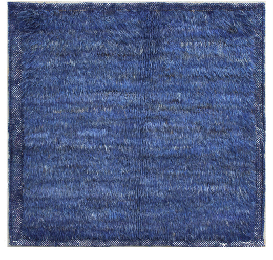 A square blue shag rug with a textured, high-pile surface and a woven border, shown flat against a white background. Atlantica Organics curates antique and handmade rugs, Persian, Afghan, Tibetan, Pakistani, Turkish Oushak, Kilim, Khotan, tribal and contemporary textiles for luxury interiors, homes and real estate. Our collections connect timeless craftsmanship with interior design, furniture, fine art, architecture and modern living. Explore curated rugs, collectible textiles, natural materials, cultural h