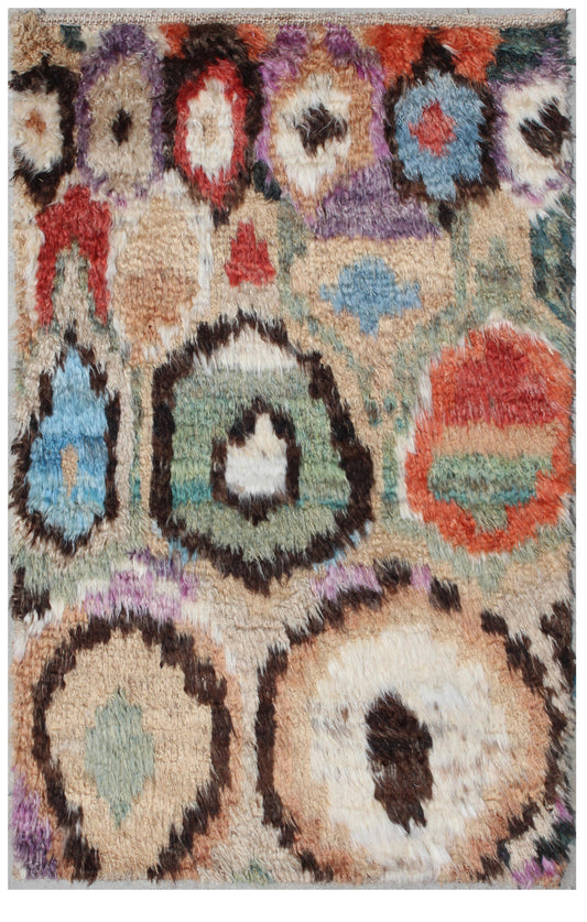 A close-up of a shaggy area rug with a multicolor abstract pattern featuring cream, beige, brown, blue, green, red, and purple motifs. Atlantica Organics curates antique and handmade rugs, Persian, Afghan, Tibetan, Pakistani, Turkish Oushak, Kilim, Khotan, tribal and contemporary textiles for luxury interiors, homes and real estate. Our collections connect timeless craftsmanship with interior design, furniture, fine art, architecture and modern living. Explore curated rugs, collectible textiles, natural mat