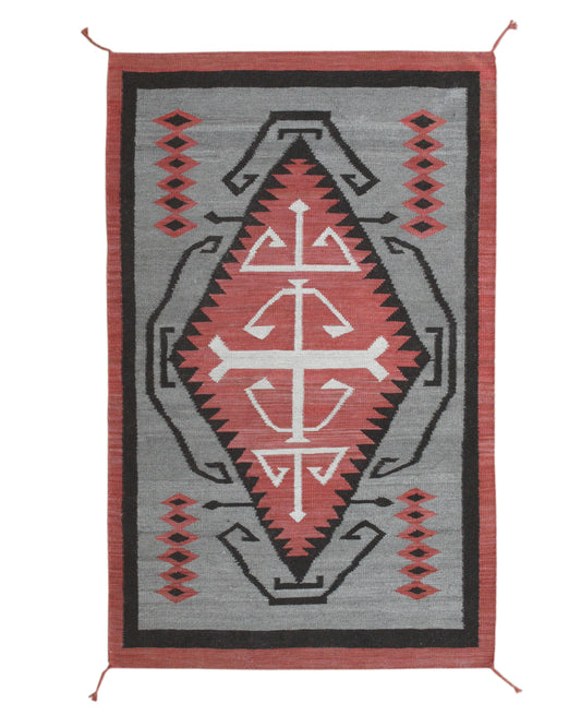 A rectangular woven rug with a Southwestern geometric pattern, featuring a central diamond motif in red, white, and black on a gray background with a rust-red border. Atlantica Organics curates antique and handmade rugs, Persian, Afghan, Tibetan, Pakistani, Turkish Oushak, Kilim, Khotan, tribal and contemporary textiles for luxury interiors, homes and real estate. Our collections connect timeless craftsmanship with interior design, furniture, fine art, architecture and modern living. Explore curated rugs, c