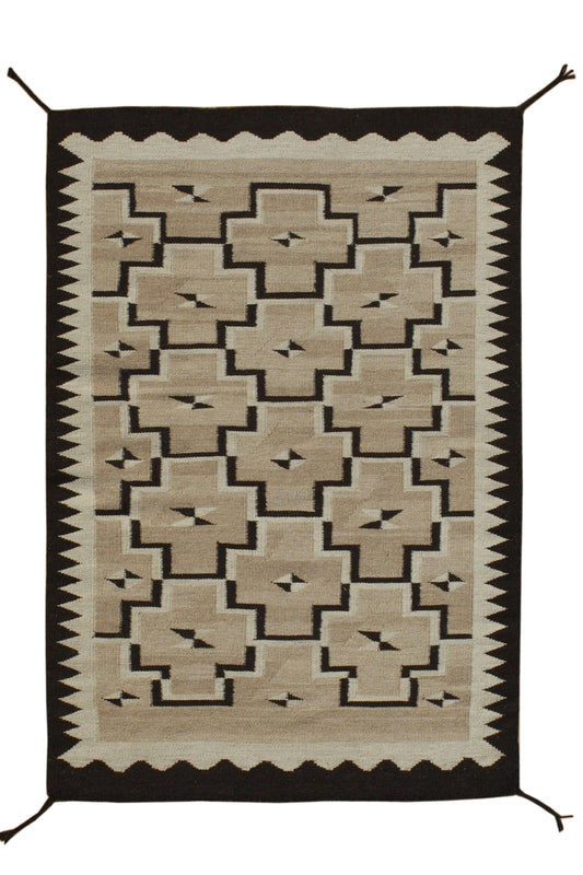 A rectangular woven rug with a Southwestern geometric pattern in beige, brown, and black, featuring hanging tassels at the corners. Atlantica Organics curates antique and handmade rugs, Persian, Afghan, Tibetan, Pakistani, Turkish Oushak, Kilim, Khotan, tribal and contemporary textiles for luxury interiors, homes and real estate. Our collections connect timeless craftsmanship with interior design, furniture, fine art, architecture and modern living. Explore curated rugs, collectible textiles, natural materi