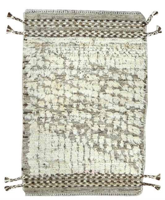 A rectangular woven rug with a textured, abstract pattern in cream, beige, and gray, featuring braided borders and tassels on the corners, shown against a plain white background.Atlantica Organics curates antique and handmade rugs, Persian, Afghan, Tibetan, Pakistani, Turkish Oushak, Kilim, Khotan, tribal and contemporary textiles for luxury interiors, homes and real estate. Our collections connect timeless craftsmanship with interior design, furniture, fine art, architecture and modern living. Explore cura