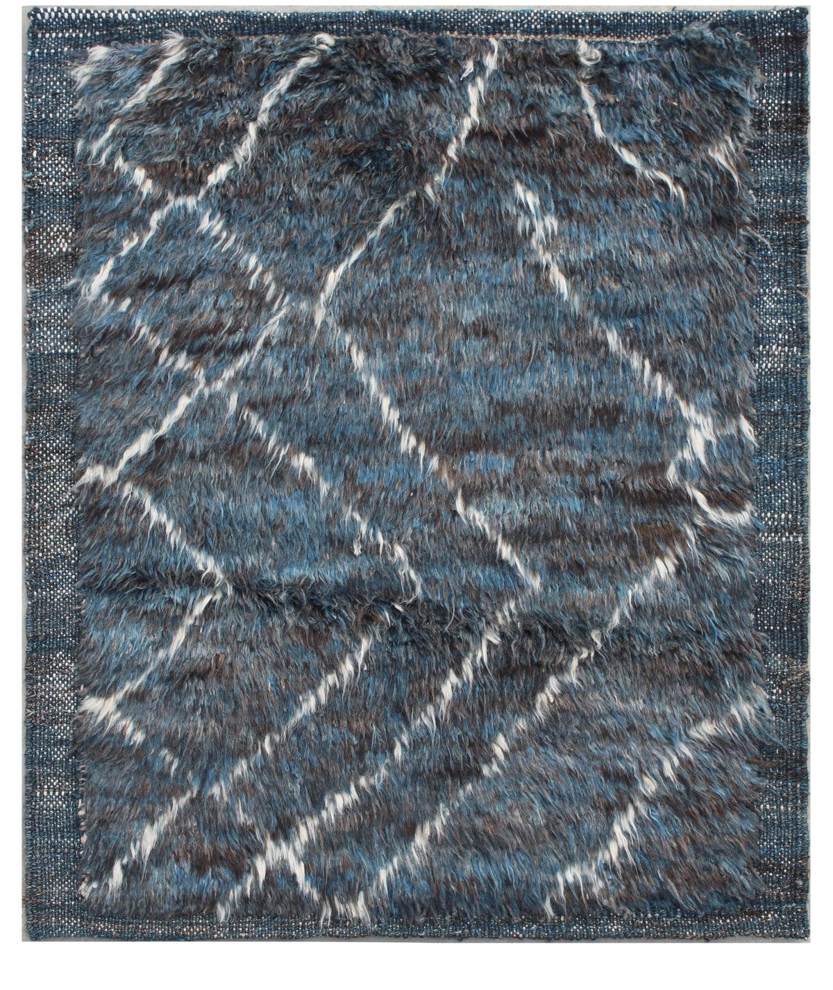 A rectangular shag area rug with a textured, fuzzy pile. The design features a geometric diamond pattern in shades of slate blue, charcoal gray, and off-white, framed by a matching blue border. Atlantica Organics curates antique and handmade rugs, Persian, Afghan, Tibetan, Pakistani, Turkish Oushak, Kilim, Khotan, tribal and contemporary textiles for luxury interiors, homes and real estate. Our collections connect timeless craftsmanship with interior design, furniture, fine art, architecture and modern livi