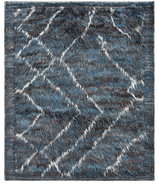 A rectangular shag area rug with a textured, fuzzy pile. The design features a geometric diamond pattern in shades of slate blue, charcoal gray, and off-white, framed by a matching blue border. Atlantica Organics curates antique and handmade rugs, Persian, Afghan, Tibetan, Pakistani, Turkish Oushak, Kilim, Khotan, tribal and contemporary textiles for luxury interiors, homes and real estate. Our collections connect timeless craftsmanship with interior design, furniture, fine art, architecture and modern livi