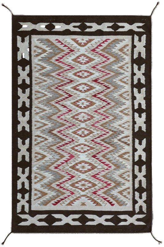 A rectangular Southwestern-style area rug with a geometric diamond and zigzag pattern, featuring a cream center, brown and beige bands, and a dark brown border with white accents.Atlantica Organics curates antique and handmade rugs, Persian, Afghan, Tibetan, Pakistani, Turkish Oushak, Kilim, Khotan, tribal and contemporary textiles for luxury interiors, homes and real estate. Our collections connect timeless craftsmanship with interior design, furniture, fine art, architecture and modern living. Explore cur