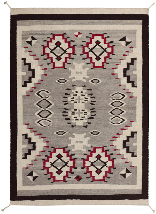 A rectangular woven area rug with a Southwestern geometric pattern, featuring a gray field, cream borders, and red, black, and white motifs. Atlantica Organics curates antique and handmade rugs, Persian, Afghan, Tibetan, Pakistani, Turkish Oushak, Kilim, Khotan, tribal and contemporary textiles for luxury interiors, homes and real estate. Our collections connect timeless craftsmanship with interior design, furniture, fine art, architecture and modern living. Explore curated rugs, collectible textiles, natur