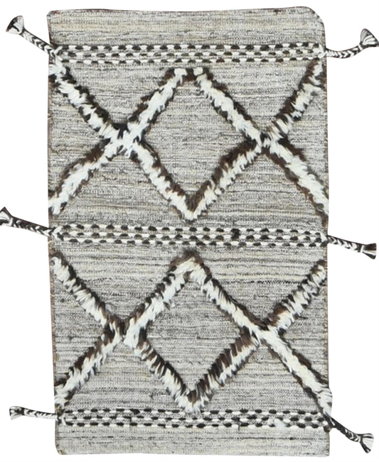 A rectangular woven rug with a textured gray and white base, featuring a bold geometric diamond pattern in white and dark brown, finished with decorative tassels on the corners and sides.Atlantica Organics curates antique and handmade rugs, Persian, Afghan, Tibetan, Pakistani, Turkish Oushak, Kilim, Khotan, tribal and contemporary textiles for luxury interiors, homes and real estate. Our collections connect timeless craftsmanship with interior design, furniture, fine art, architecture and modern living. Exp