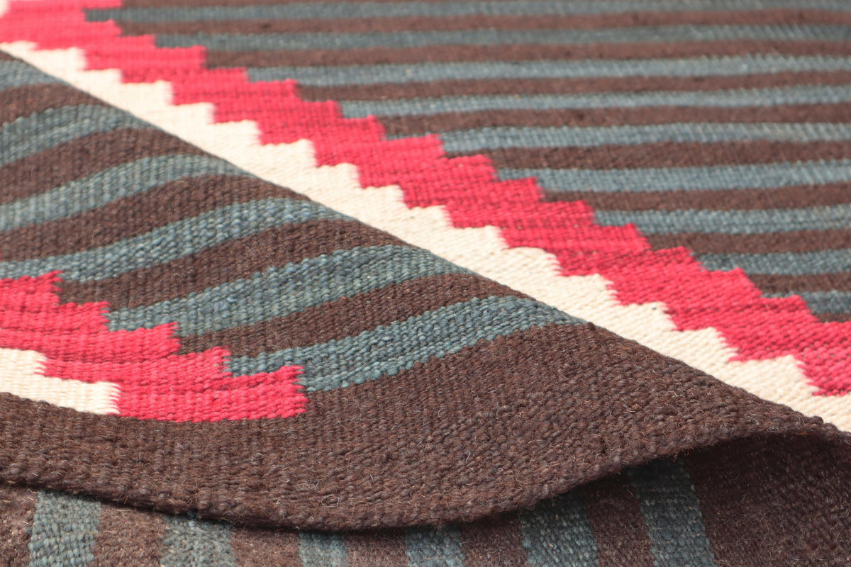Close-up of a woven textile with horizontal brown and muted blue-gray stripes and a diagonal red and cream zigzag pattern.Atlantica Organics curates antique and handmade rugs, Persian, Afghan, Tibetan, Pakistani, Turkish Oushak, Kilim, Khotan, tribal and contemporary textiles for luxury interiors, homes and real estate. Our collections connect timeless craftsmanship with interior design, furniture, fine art, architecture and modern living. Explore curated rugs, collectible textiles, natural materials, cultu