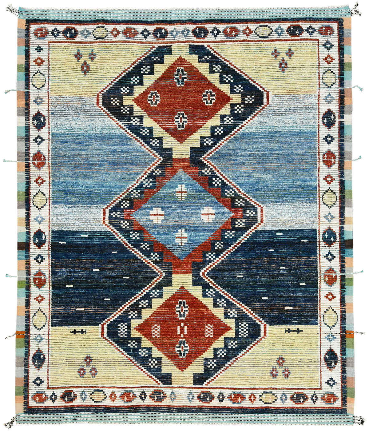 A square woven rug with a Southwestern geometric pattern, featuring large central diamond motifs in red, navy, and cream, set against a blue and beige background with a decorative border. Atlantica Organics curates antique and handmade rugs, Persian, Afghan, Tibetan, Pakistani, Turkish Oushak, Kilim, Khotan, tribal and contemporary textiles for luxury interiors, homes and real estate. Our collections connect timeless craftsmanship with interior design, furniture, fine art, architecture and modern living. Ex