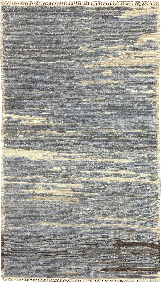 A rectangular area rug with a distressed, horizontal textured pattern in shades of slate blue, gray, and cream.Atlantica Organics curates antique and handmade rugs, Persian, Afghan, Tibetan, Pakistani, Turkish Oushak, Kilim, Khotan, tribal and contemporary textiles for luxury interiors, homes and real estate. Our collections connect timeless craftsmanship with interior design, furniture, fine art, architecture and modern living. Explore curated rugs, collectible textiles, natural materials, cultural heritag