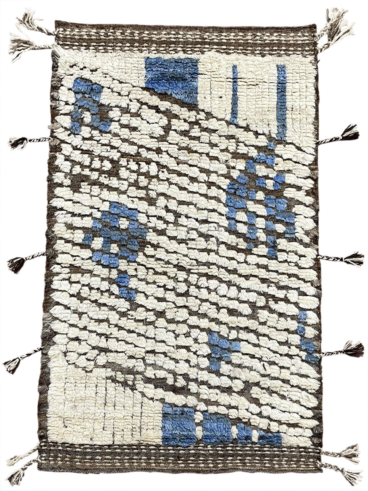 A rectangular handwoven rug with a textured abstract pattern in cream, blue, and dark brown, finished with tassel fringe on all sides.Atlantica Organics curates antique and handmade rugs, Persian, Afghan, Tibetan, Pakistani, Turkish Oushak, Kilim, Khotan, tribal and contemporary textiles for luxury interiors, homes and real estate. Our collections connect timeless craftsmanship with interior design, furniture, fine art, architecture and modern living. Explore curated rugs, collectible textiles, natural mate
