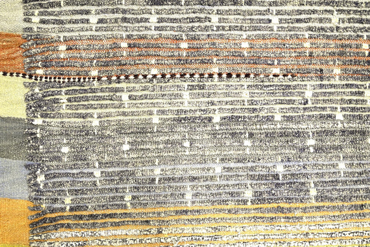A close-up of a woven textile or rug showing horizontal striped patterns in gray, black, white, rust orange, and mustard yellow. Atlantica Organics curates antique and handmade rugs, Persian, Afghan, Tibetan, Pakistani, Turkish Oushak, Kilim, Khotan, tribal and contemporary textiles for luxury interiors, homes and real estate. Our collections connect timeless craftsmanship with interior design, furniture, fine art, architecture and modern living. Explore curated rugs, collectible textiles, natural materials