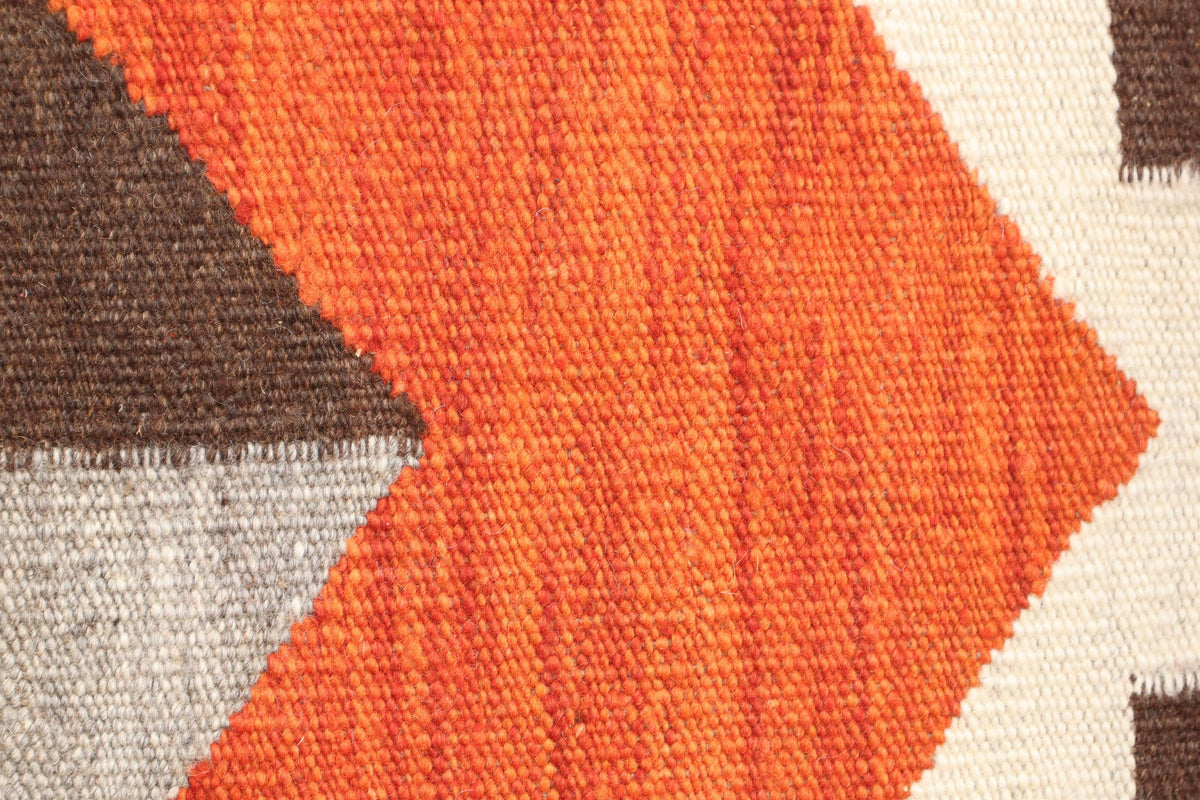Close-up of a woven textile pattern with a large orange chevron shape over brown, light gray, and off-white geometric sections.Atlantica Organics curates antique and handmade rugs, Persian, Afghan, Tibetan, Pakistani, Turkish Oushak, Kilim, Khotan, tribal and contemporary textiles for luxury interiors, homes and real estate. Our collections connect timeless craftsmanship with interior design, furniture, fine art, architecture and modern living. Explore curated rugs, collectible textiles, natural materials, 