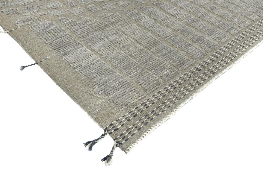 A close-up of a woven rug corner showing a textured taupe and gray striped pattern with black and gray fringe tassels on a white background. Atlantica Organics curates antique and handmade rugs, Persian, Afghan, Tibetan, Pakistani, Turkish Oushak, Kilim, Khotan, tribal and contemporary textiles for luxury interiors, homes and real estate. Our collections connect timeless craftsmanship with interior design, furniture, fine art, architecture and modern living. Explore curated rugs, collectible textiles, natur