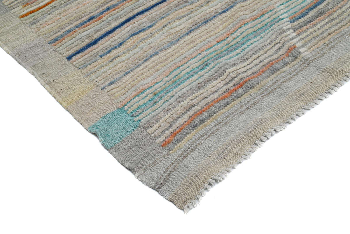A close-up of a woven rug corner showing a textured striped pattern in beige, gray, blue, and orange on a white background. Atlantica Organics curates antique and handmade rugs, Persian, Afghan, Tibetan, Pakistani, Turkish Oushak, Kilim, Khotan, tribal and contemporary textiles for luxury interiors, homes and real estate. Our collections connect timeless craftsmanship with interior design, furniture, fine art, architecture and modern living. Explore curated rugs, collectible textiles, natural materials, cul