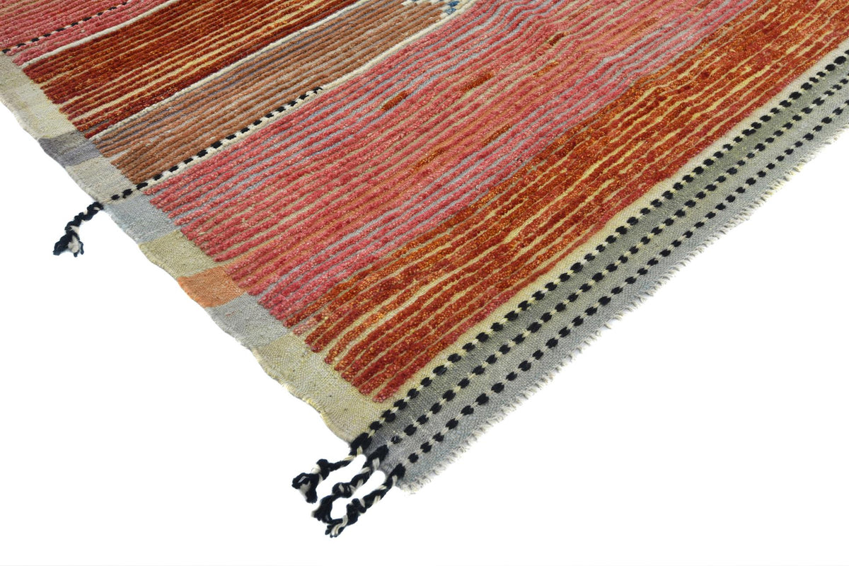 A close-up of a woven rug corner showing a striped pattern in rust red, terracotta, peach, beige, and gray with black dotted border details and black tassels on a white background. Atlantica Organics curates antique and handmade rugs, Persian, Afghan, Tibetan, Pakistani, Turkish Oushak, Kilim, Khotan, tribal and contemporary textiles for luxury interiors, homes and real estate. Our collections connect timeless craftsmanship with interior design, furniture, fine art, architecture and modern living. Explore c