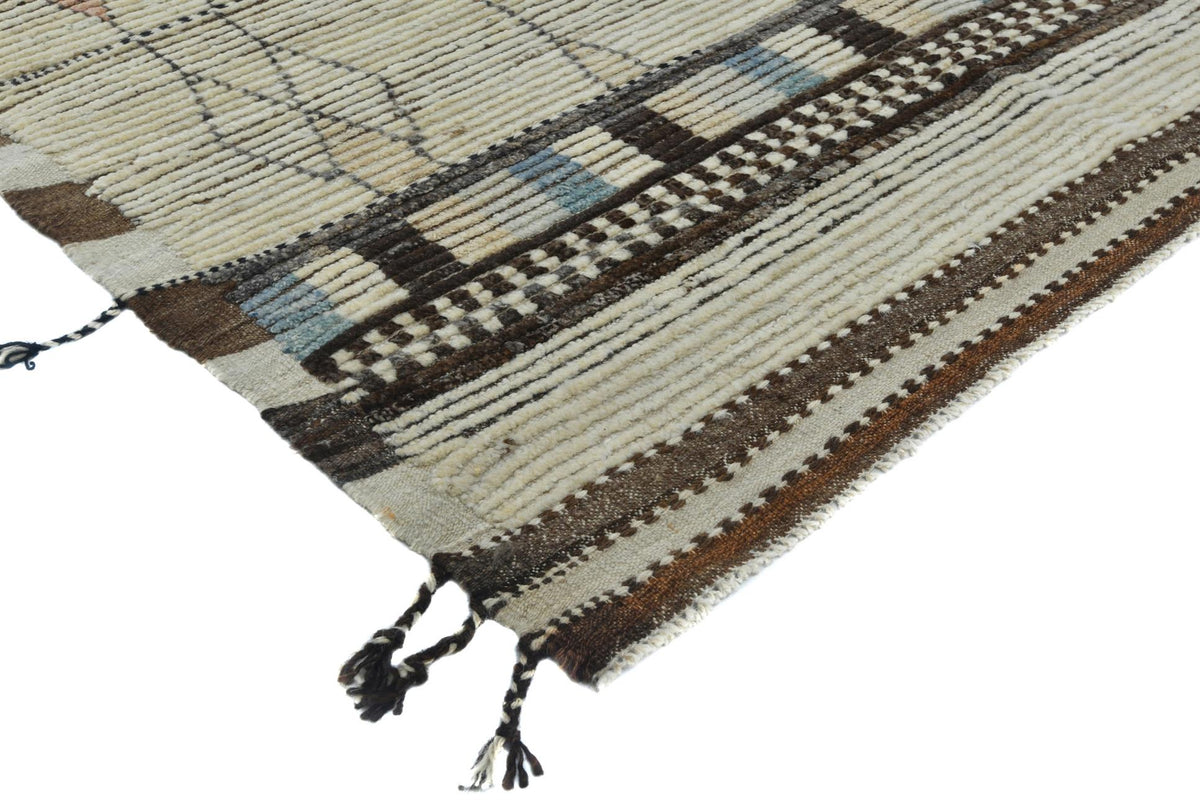A close-up of a woven rug corner showing cream, brown, and black geometric stripes with small light blue accents and black tassels on a white background. Atlantica Organics curates antique and handmade rugs, Persian, Afghan, Tibetan, Pakistani, Turkish Oushak, Kilim, Khotan, tribal and contemporary textiles for luxury interiors, homes and real estate. Our collections connect timeless craftsmanship with interior design, furniture, fine art, architecture and modern living. Explore curated rugs, collectible te
