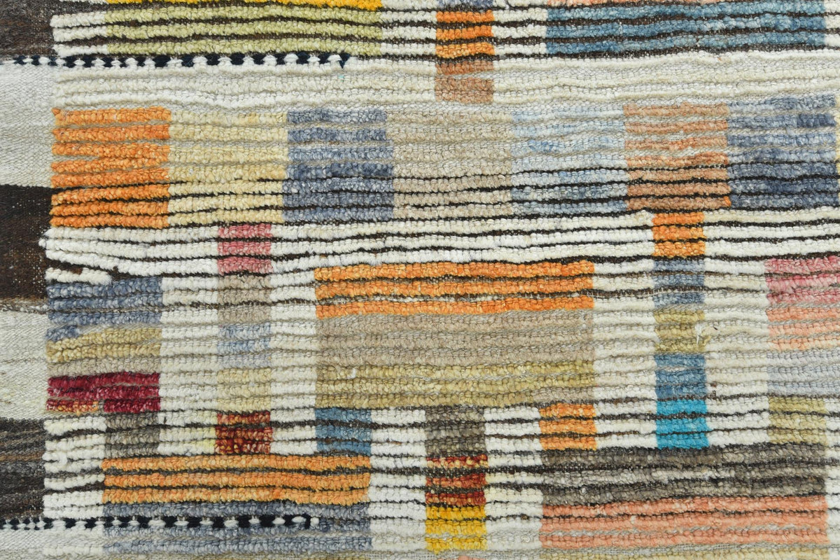 A close-up of a textured woven rug with a geometric pattern in beige, orange, blue, gray, brown, and red. Atlantica Organics curates antique and handmade rugs, Persian, Afghan, Tibetan, Pakistani, Turkish Oushak, Kilim, Khotan, tribal and contemporary textiles for luxury interiors, homes and real estate. Our collections connect timeless craftsmanship with interior design, furniture, fine art, architecture and modern living. Explore curated rugs, collectible textiles, natural materials, cultural heritage, su