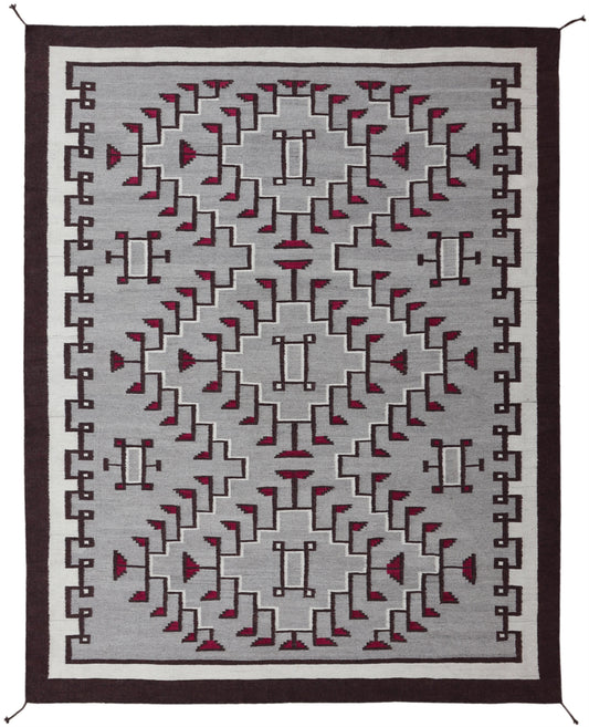 A rectangular area rug with a geometric Southwestern-style pattern, featuring a gray field with red and black motifs, bordered by white and dark brown frames. Atlantica Organics curates antique and handmade rugs, Persian, Afghan, Tibetan, Pakistani, Turkish Oushak, Kilim, Khotan, tribal and contemporary textiles for luxury interiors, homes and real estate. Our collections connect timeless craftsmanship with interior design, furniture, fine art, architecture and modern living. Explore curated rugs, collectib