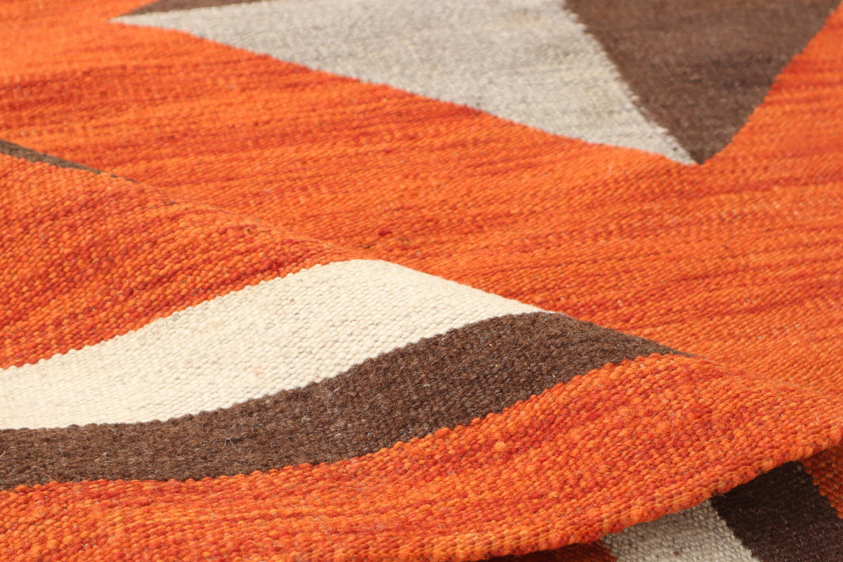 Close-up of a woven textile with a geometric pattern in bright orange, cream, brown, and light gray.Atlantica Organics curates antique and handmade rugs, Persian, Afghan, Tibetan, Pakistani, Turkish Oushak, Kilim, Khotan, tribal and contemporary textiles for luxury interiors, homes and real estate. Our collections connect timeless craftsmanship with interior design, furniture, fine art, architecture and modern living. Explore curated rugs, collectible textiles, natural materials, cultural heritage, sustaina