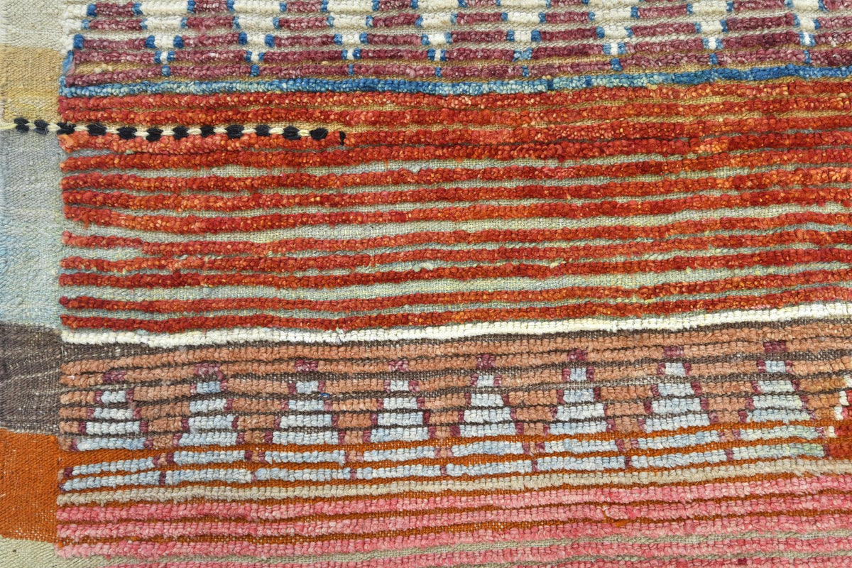 Close-up of a woven textile or rug showing horizontal bands with geometric patterns in rust red, terracotta, pink, beige, brown, and small blue accents. Atlantica Organics curates antique and handmade rugs, Persian, Afghan, Tibetan, Pakistani, Turkish Oushak, Kilim, Khotan, tribal and contemporary textiles for luxury interiors, homes and real estate. Our collections connect timeless craftsmanship with interior design, furniture, fine art, architecture and modern living. Explore curated rugs, collectible tex