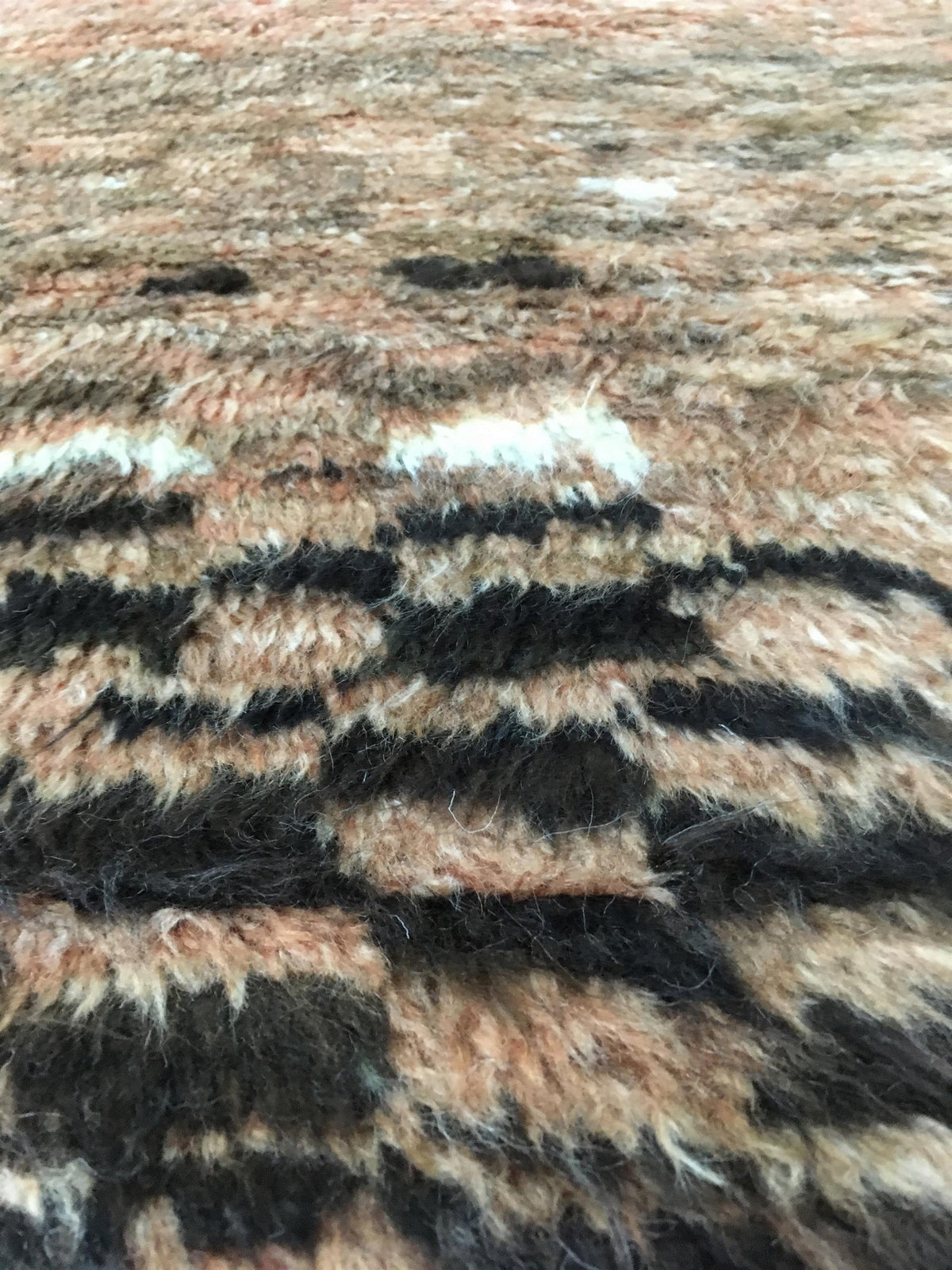 Close-up of a textured, shaggy woven rug with a pattern of black, beige, and white stripes. Atlantica Organics curates antique and handmade rugs, Persian, Afghan, Tibetan, Pakistani, Turkish Oushak, Kilim, Khotan, tribal and contemporary textiles for luxury interiors, homes and real estate. Our collections connect timeless craftsmanship with interior design, furniture, fine art, architecture and modern living. Explore curated rugs, collectible textiles, natural materials, cultural heritage, sustainable desi