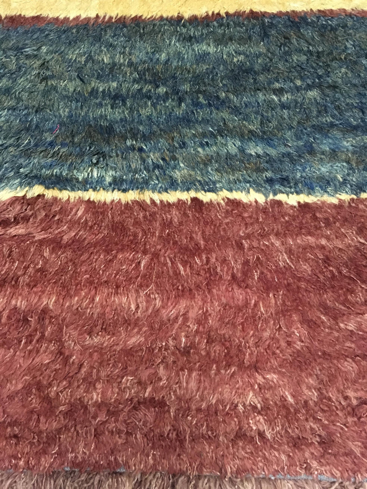 A close-up of a shaggy, high-pile rug with horizontal stripes in blue, rust red, and cream. Atlantica Organics curates antique and handmade rugs, Persian, Afghan, Tibetan, Pakistani, Turkish Oushak, Kilim, Khotan, tribal and contemporary textiles for luxury interiors, homes and real estate. Our collections connect timeless craftsmanship with interior design, furniture, fine art, architecture and modern living. Explore curated rugs, collectible textiles, natural materials, cultural heritage, sustainable desi