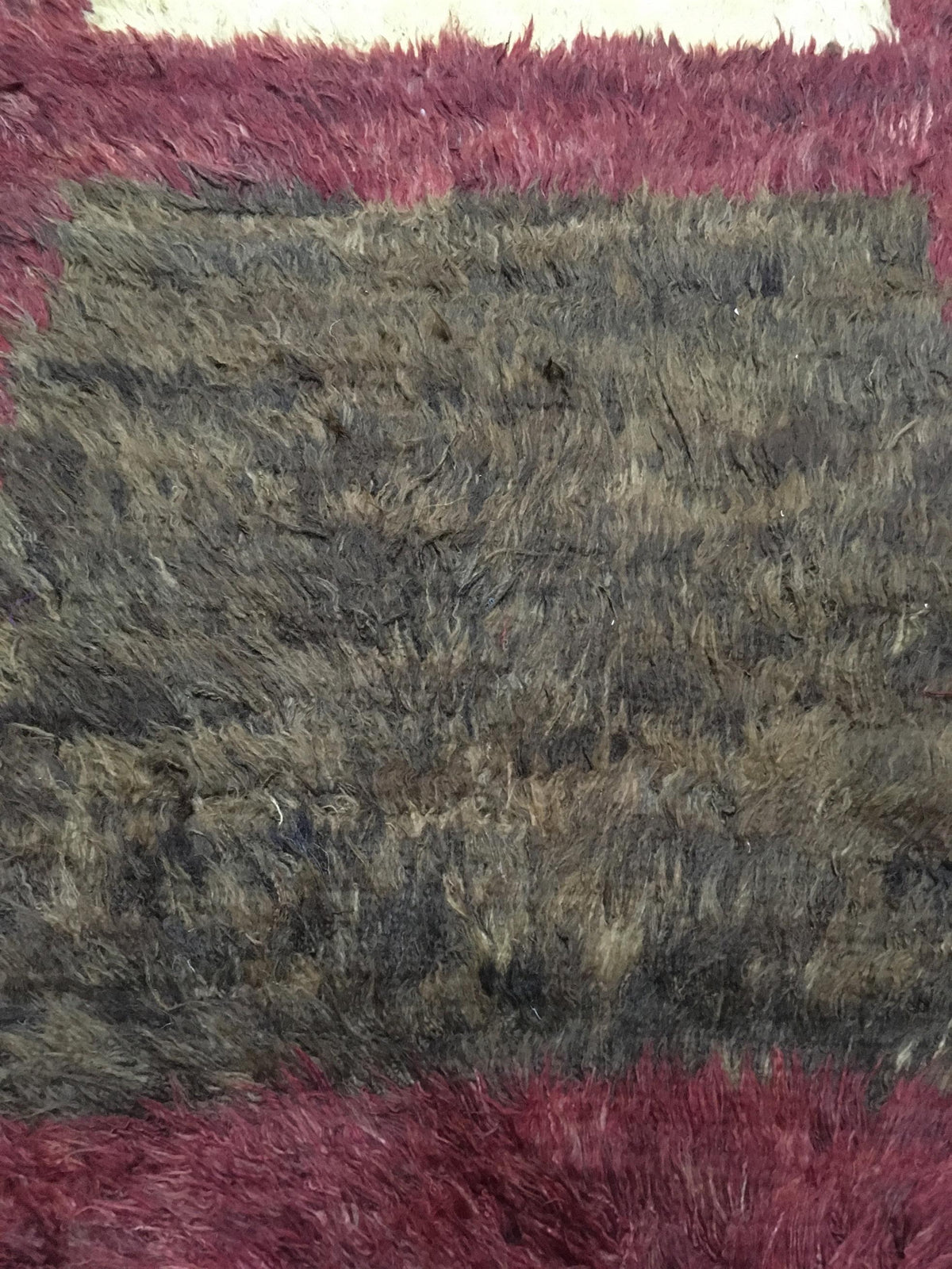 A close-up of a shaggy, high-pile rug with a textured center in charcoal gray and brown tones, bordered by dusty rose pink sections at the top and bottom. Atlantica Organics curates antique and handmade rugs, Persian, Afghan, Tibetan, Pakistani, Turkish Oushak, Kilim, Khotan, tribal and contemporary textiles for luxury interiors, homes and real estate. Our collections connect timeless craftsmanship with interior design, furniture, fine art, architecture and modern living. Explore curated rugs, collectible t