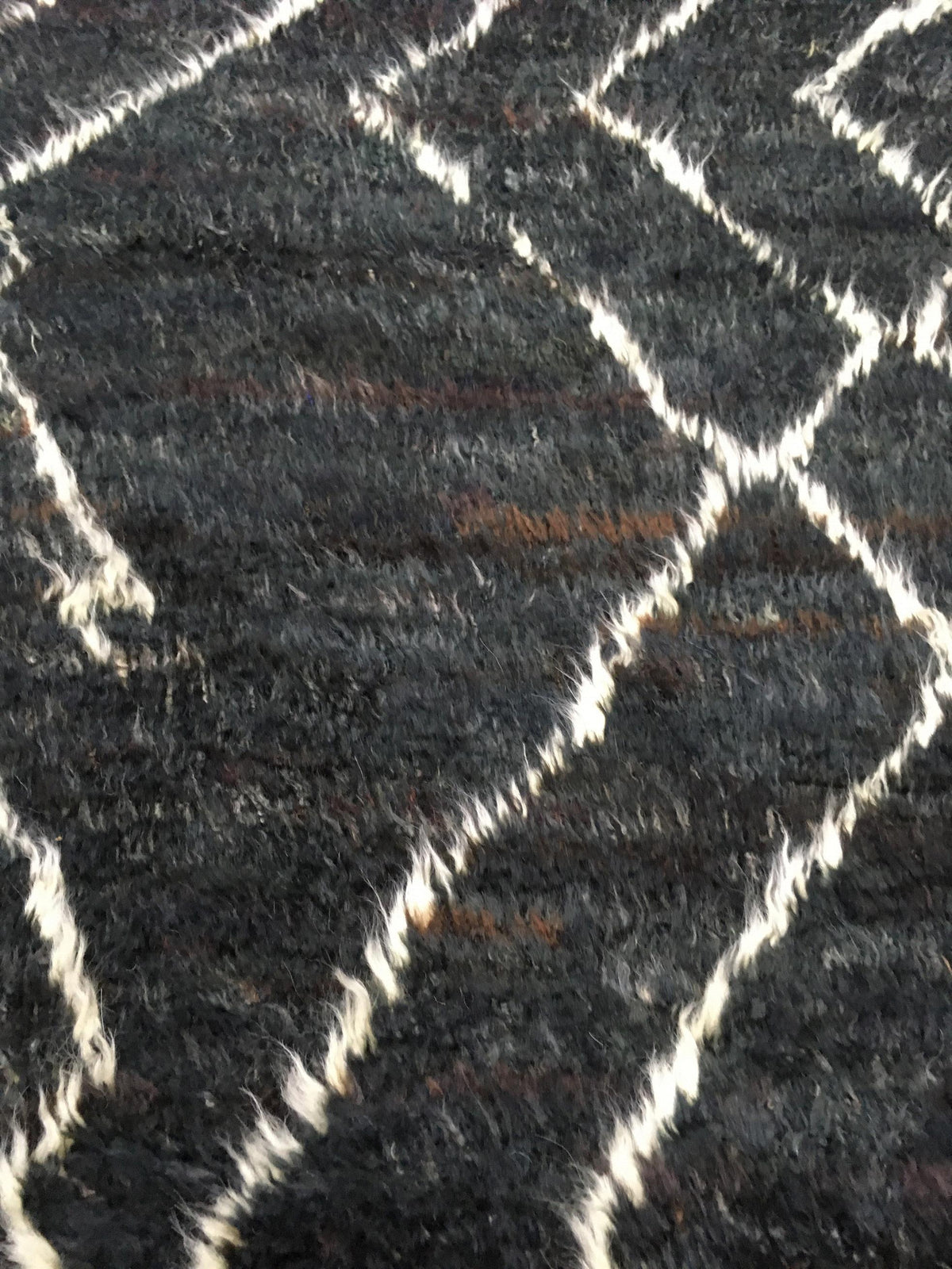 A close-up of a textured black shag rug with a cream-colored geometric diamond pattern. Atlantica Organics curates antique and handmade rugs, Persian, Afghan, Tibetan, Pakistani, Turkish Oushak, Kilim, Khotan, tribal and contemporary textiles for luxury interiors, homes and real estate. Our collections connect timeless craftsmanship with interior design, furniture, fine art, architecture and modern living. Explore curated rugs, collectible textiles, natural materials, cultural heritage, sustainable design a