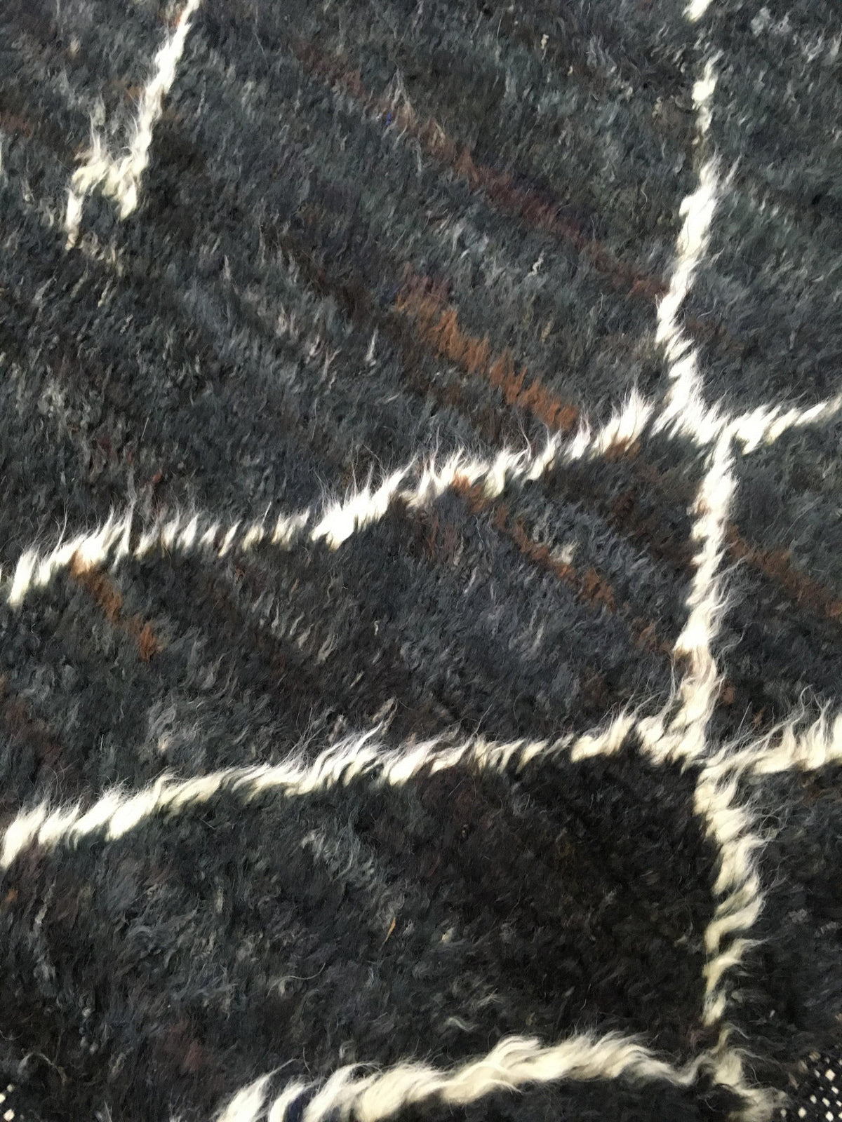 A close-up of a textured black and dark gray shaggy rug with a white grid pattern.Atlantica Organics curates antique and handmade rugs, Persian, Afghan, Tibetan, Pakistani, Turkish Oushak, Kilim, Khotan, tribal and contemporary textiles for luxury interiors, homes and real estate. Our collections connect timeless craftsmanship with interior design, furniture, fine art, architecture and modern living. Explore curated rugs, collectible textiles, natural materials, cultural heritage, sustainable design and dis