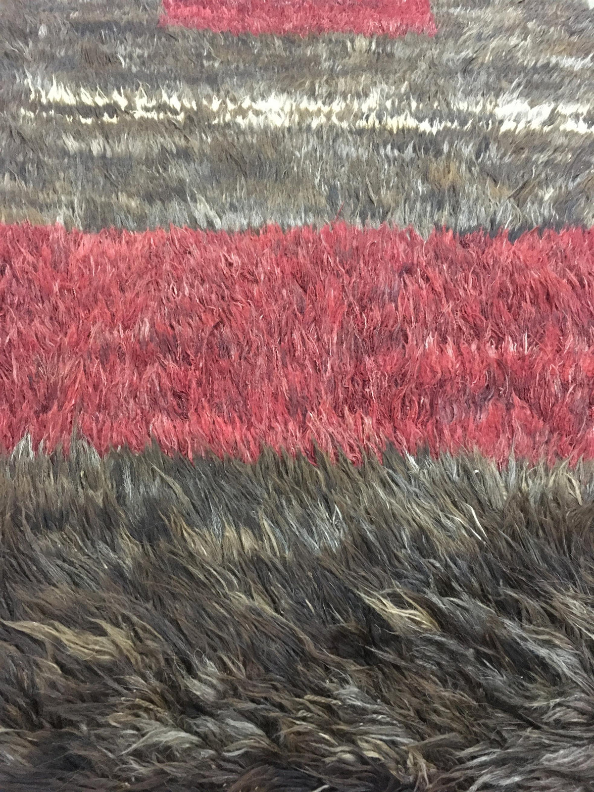 A close-up of a shaggy faux fur rug with horizontal stripes in vibrant red, dark brown, and gray. Atlantica Organics curates antique and handmade rugs, Persian, Afghan, Tibetan, Pakistani, Turkish Oushak, Kilim, Khotan, tribal and contemporary textiles for luxury interiors, homes and real estate. Our collections connect timeless craftsmanship with interior design, furniture, fine art, architecture and modern living. Explore curated rugs, collectible textiles, natural materials, cultural heritage, sustainabl
