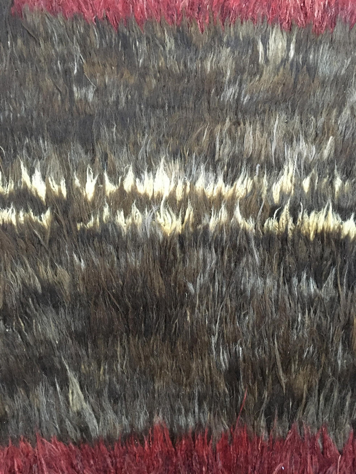 A close-up of a shaggy faux fur fabric with horizontal stripes in dark brown, black, cream, and deep red. Atlantica Organics curates antique and handmade rugs, Persian, Afghan, Tibetan, Pakistani, Turkish Oushak, Kilim, Khotan, tribal and contemporary textiles for luxury interiors, homes and real estate. Our collections connect timeless craftsmanship with interior design, furniture, fine art, architecture and modern living. Explore curated rugs, collectible textiles, natural materials, cultural heritage, su