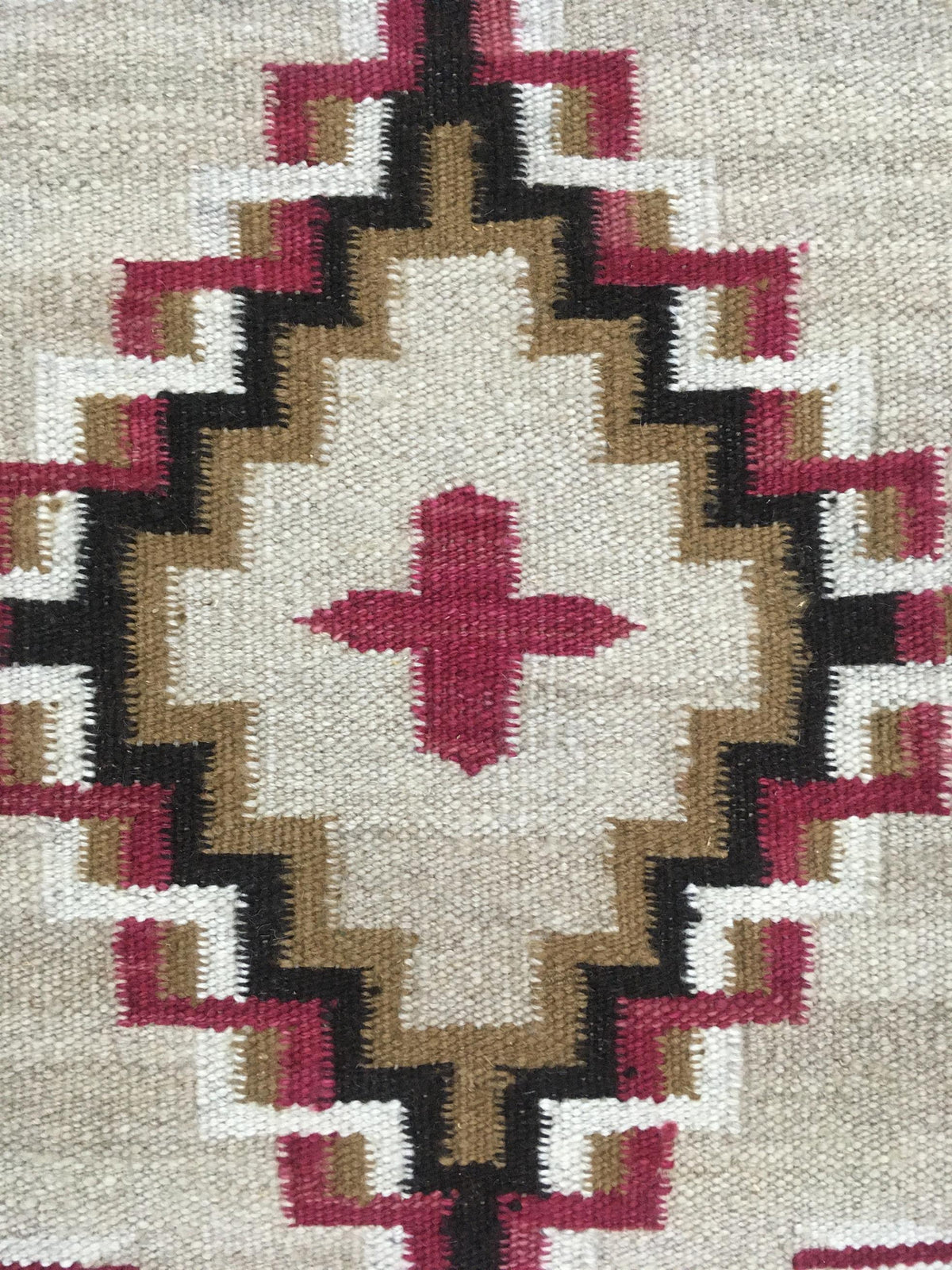 Close-up of a woven textile with a geometric Southwestern-style diamond pattern in cream, tan, black, and deep magenta. Atlantica Organics curates antique and handmade rugs, Persian, Afghan, Tibetan, Pakistani, Turkish Oushak, Kilim, Khotan, tribal and contemporary textiles for luxury interiors, homes and real estate. Our collections connect timeless craftsmanship with interior design, furniture, fine art, architecture and modern living. Explore curated rugs, collectible textiles, natural materials, cultura