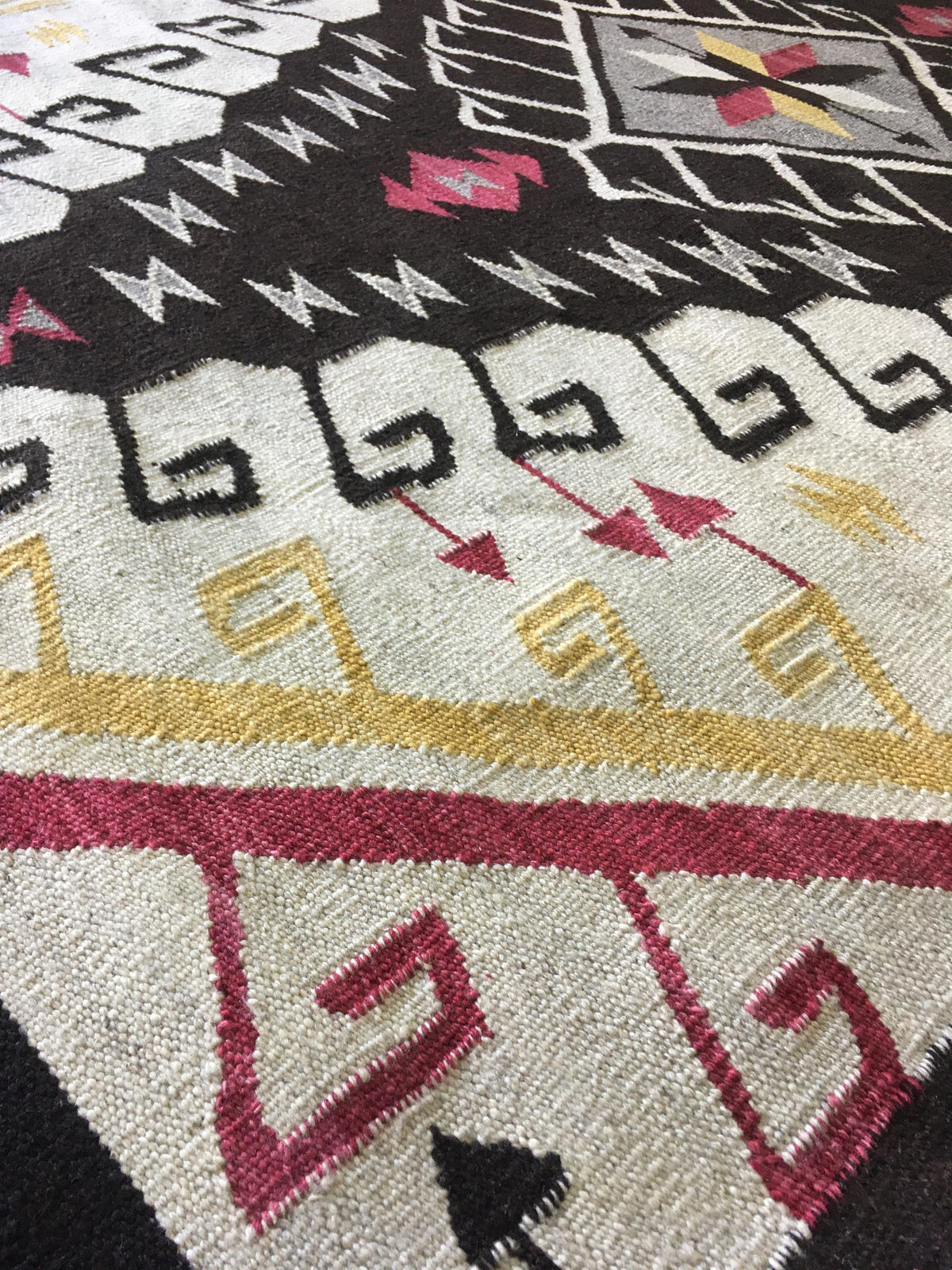 Close-up of a woven rug with a Southwestern geometric pattern in black, cream, yellow, and magenta. Atlantica Organics curates antique and handmade rugs, Persian, Afghan, Tibetan, Pakistani, Turkish Oushak, Kilim, Khotan, tribal and contemporary textiles for luxury interiors, homes and real estate. Our collections connect timeless craftsmanship with interior design, furniture, fine art, architecture and modern living. Explore curated rugs, collectible textiles, natural materials, cultural heritage, sustaina