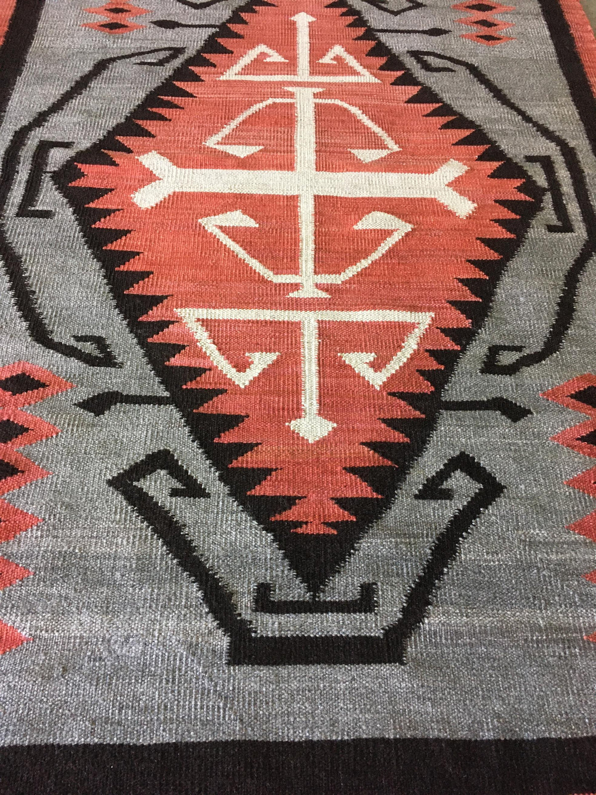 A close-up of a woven textile with a geometric Southwestern-style pattern in gray, rust red, black, and off-white.Atlantica Organics curates antique and handmade rugs, Persian, Afghan, Tibetan, Pakistani, Turkish Oushak, Kilim, Khotan, tribal and contemporary textiles for luxury interiors, homes and real estate. Our collections connect timeless craftsmanship with interior design, furniture, fine art, architecture and modern living. Explore curated rugs, collectible textiles, natural materials, cultural heri