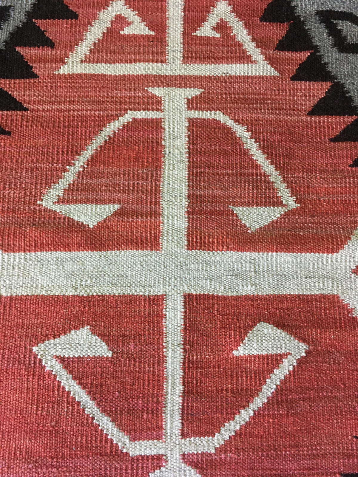 Close-up of a woven textile with a geometric Southwestern-style pattern in terracotta red, off-white, and black. Atlantica Organics curates antique and handmade rugs, Persian, Afghan, Tibetan, Pakistani, Turkish Oushak, Kilim, Khotan, tribal and contemporary textiles for luxury interiors, homes and real estate. Our collections connect timeless craftsmanship with interior design, furniture, fine art, architecture and modern living. Explore curated rugs, collectible textiles, natural materials, cultural herit