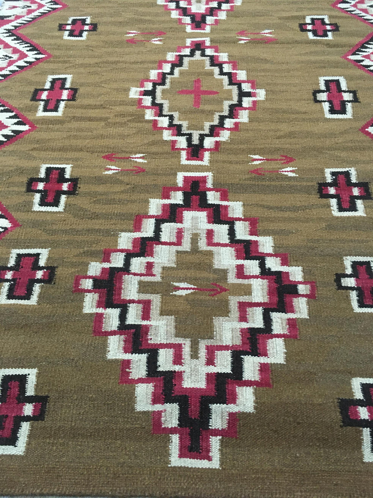 A close-up of a woven rug with a Southwestern geometric pattern in brown, pink, white, and black. Atlantica Organics curates antique and handmade rugs, Persian, Afghan, Tibetan, Pakistani, Turkish Oushak, Kilim, Khotan, tribal and contemporary textiles for luxury interiors, homes and real estate. Our collections connect timeless craftsmanship with interior design, furniture, fine art, architecture and modern living. Explore curated rugs, collectible textiles, natural materials, cultural heritage, sustainabl