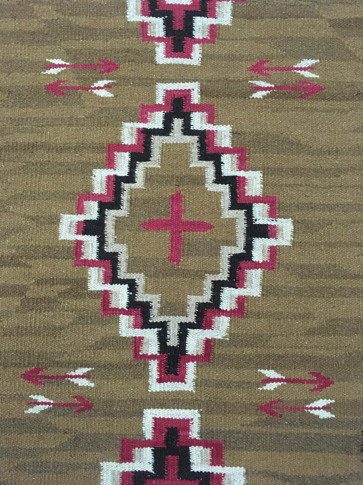 A close-up of a woven textile or rug showing a geometric Southwestern-style pattern in olive brown, magenta pink, black, and white. Atlantica Organics curates antique and handmade rugs, Persian, Afghan, Tibetan, Pakistani, Turkish Oushak, Kilim, Khotan, tribal and contemporary textiles for luxury interiors, homes and real estate. Our collections connect timeless craftsmanship with interior design, furniture, fine art, architecture and modern living. Explore curated rugs, collectible textiles, natural materi