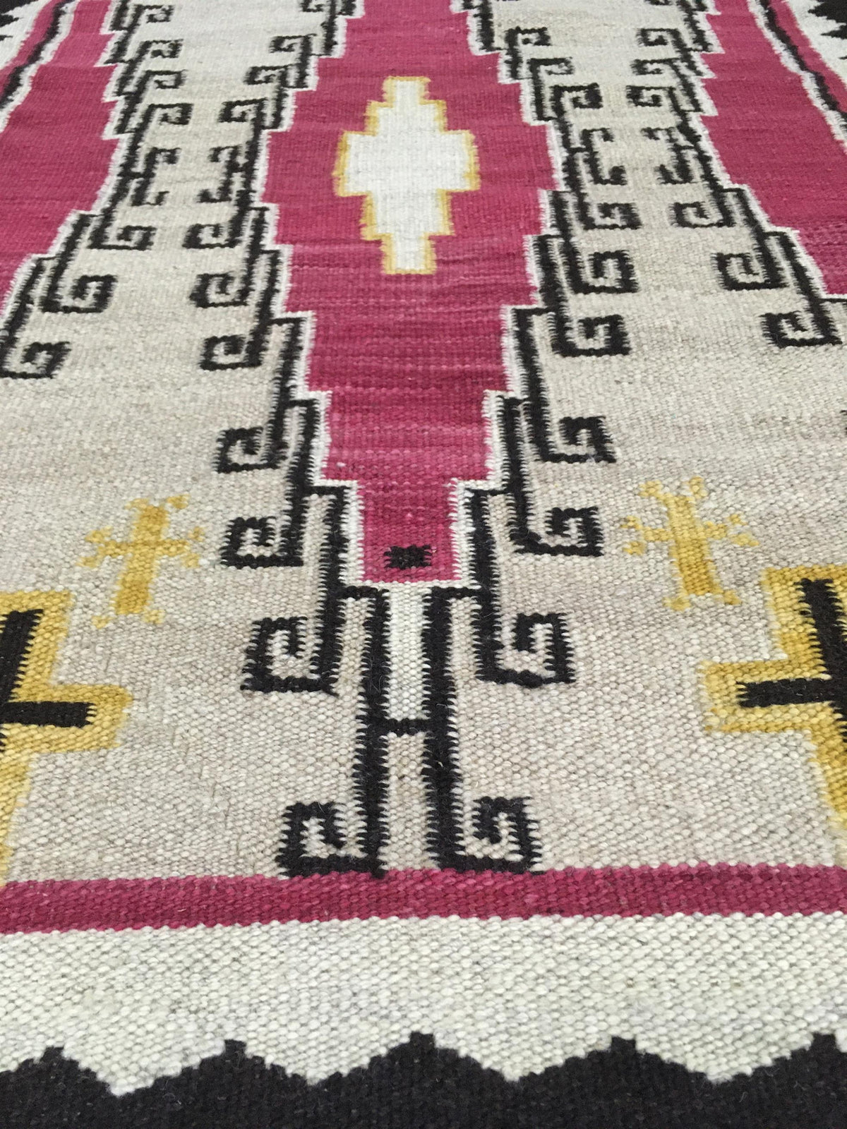 A close-up of a woven rug with a geometric Southwestern pattern in pink, cream, black, and yellow.Atlantica Organics curates antique and handmade rugs, Persian, Afghan, Tibetan, Pakistani, Turkish Oushak, Kilim, Khotan, tribal and contemporary textiles for luxury interiors, homes and real estate. Our collections connect timeless craftsmanship with interior design, furniture, fine art, architecture and modern living. Explore curated rugs, collectible textiles, natural materials, cultural heritage, sustainabl